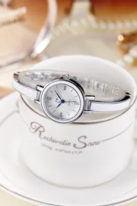 Détail d'une montre femme en argent avec chiffres romains et bracelet rigide sur tasse