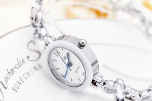 Close-up of silver clover-shaped metal strap and white dial of a ladies quartz watch