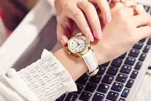 Close-up of women's quartz watch with white leather strap and gold case on wrist