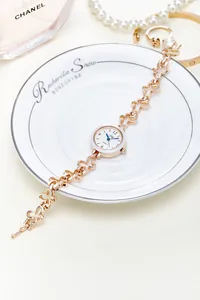 Detail of rose gold clover bracelet watch on porcelain dish with elegant accessories
