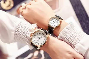 Detail of couple wearing gold quartz watches with white dials and black leather straps