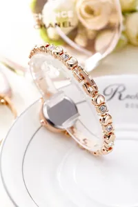 Macro shot of rose gold fashion watch with heart-shaped crystal links on white plate