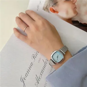 Détail d'une montre carrée argentée avec cadran bleu clair et bracelet en maille au poignet