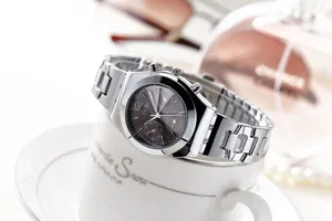 Silver stainless steel watch with grey dial resting on a white coffee cup edge