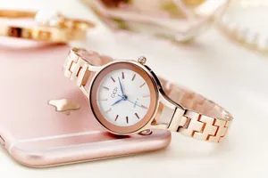 Detailed close-up of a rose gold women's steel watch with textured white dial and luxury accessories