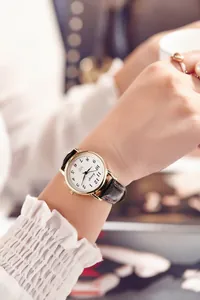 Close-up of hosiqi quartz watch with gold case and black leather strap on wrist