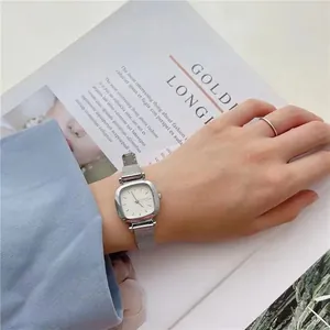 Montre carrée argentée avec bracelet en maille milanaise portée sur fond de magazine
