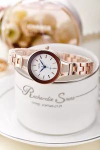 Close-up of rose gold watch with blue hands resting on a white ceramic coffee cup