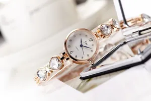 Makro-Detail einer roségoldenen Herz-Armbanduhr mit Kristallen auf einer Spiegelfläche