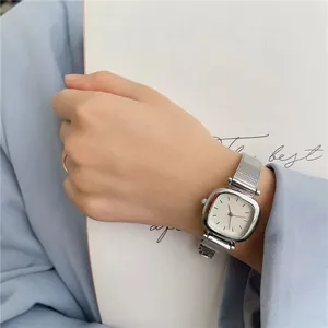 Montre carrée argentée élégante avec bracelet en maille sur poignet féminin fond bleu