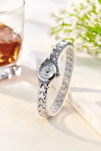 Elegant silver quartz watch with white dial and rhinestone markers on minimalist book