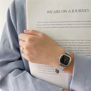 Gros plan d'une montre carrée argentée avec cadran noir et bracelet en maille milanaise