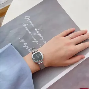 Détail de la montre carrée argentée avec cadran noir et bracelet en maille milanaise