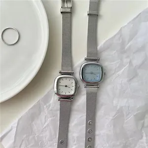 Détail de montres carrées argentées minimalistes avec bracelets en maille sur fond blanc