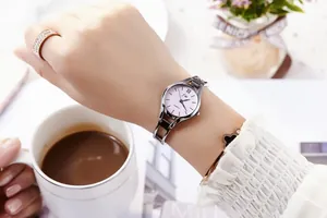 Close-up of a silver steel strap watch with a purple dial worn with elegant jewelry