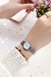 Close-up of a women's silver mesh watch paired with a rose gold clover bracelet