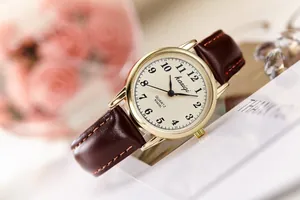 Close-up of retro quartz watch with cream dial and brown leather strap on floral background