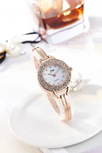 Macro detail of rose gold bracelet watch dial with crystal bezel and pearl background