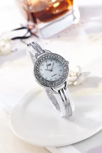 Detail of silver quartz watch with diamond bezel and minimalist bangle strap on table