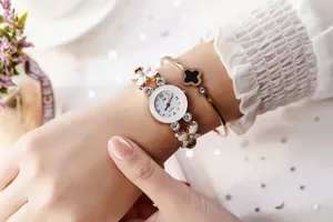 Détail de la montre bracelet dorée élégante avec breloques fleurs blanches et strass