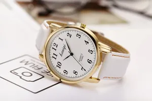 Detail of quartz watch with gold metal case, white leather strap and orange stitching