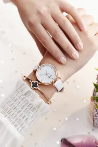Gros plan de la montre or rose élégante avec bracelet cuir blanc et parure trèfle