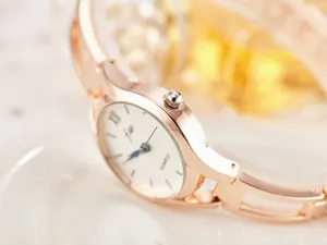 Close-up of rose gold watch case with Roman numeral dial and blue hands detail