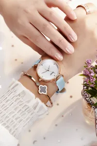 Gros plan d'une montre en or rose avec bracelet en cuir bleu clair et bracelet trèfle