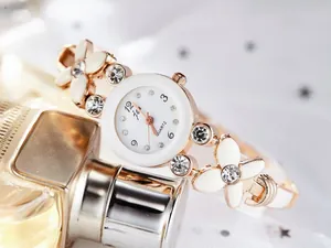 Détail de la montre bracelet fleurie avec strass posée sur un flacon de parfum