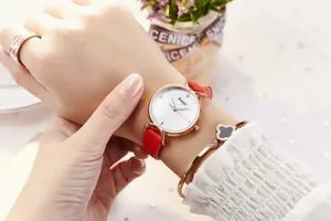 Détail de montre élégante pour femme en or rose avec bracelet cuir rouge et trèfle