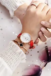 Gros plan d'une montre à bracelet en cuir rouge avec un bracelet trèfle en or rose assorti