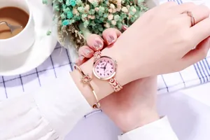 Détail d'une montre à quartz rose doré avec cadran rose et bijoux sur nappe à carreaux
