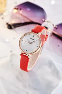 Détail d'une montre à bracelet en cuir rouge et boîtier or rose sur marbre blanc