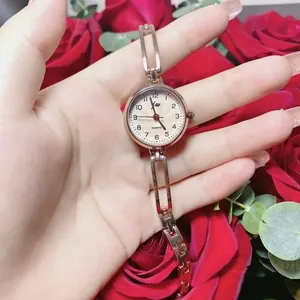 Detailed view of women's rose gold quartz watch worn on wrist with red rose background