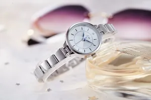 Close-up of elegant silver quartz watch with chain strap next to perfume and glasses