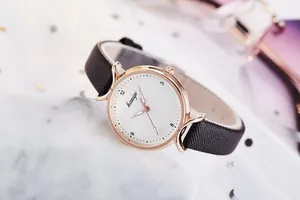 Gros plan d'une montre femme avec cadran blanc, boîtier or rose et bracelet cuir noir