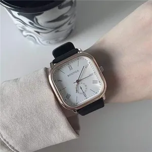 Macro detail of a square rose gold quartz watch with Roman numerals on a black leather strap