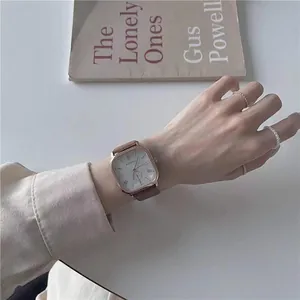 Close-up of a vintage square gold watch with a brown leather strap on a woman wrist