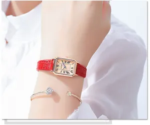 Detail view of a rose gold rectangular watch with red leather strap and heart bracelet
