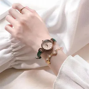 Nahaufnahme einer rotgoldenen Quarzuhr mit grünem Armband und Sternen-Charm-Armband