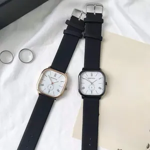 Detail of square quartz watches with Roman numeral dials and leather straps on white fabric