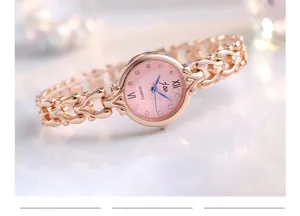 Détail de la montre or rose avec cadran rose, aiguilles bleues et index en strass sur maille