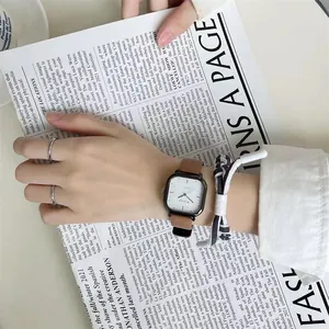 Detail einer quadratischen Quarzuhr mit braunem Lederarmband und geflochtenem Armband