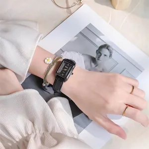 Close-up of rectangular black quartz watch with leather strap and decorative bracelets
