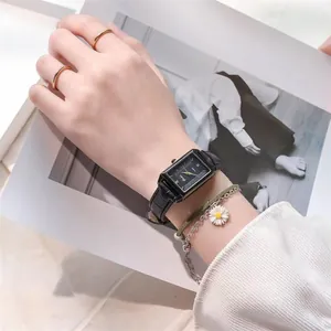 Close-up of rectangular black dial watch with gold accents and daisy bracelet on wrist
