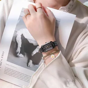 Detail of rectangular black quartz watch with leather strap and daisy chain bracelet