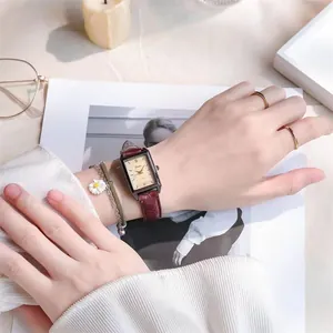 Close-up of retro square watch with burgundy leather strap and daisy bracelet on wrist