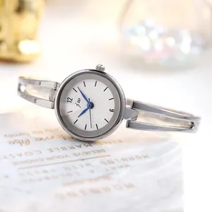 Detalle de reloj brazalete plateado con esfera blanca texturizada y agujas de metal azul