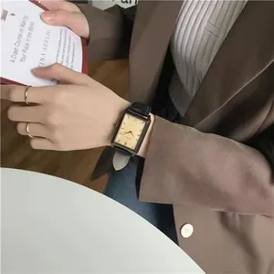 Classic rectangular gold watch with black leather strap held against a book background