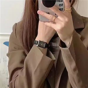 Minimalist rectangular black watch with leather strap and golden rings on wrist